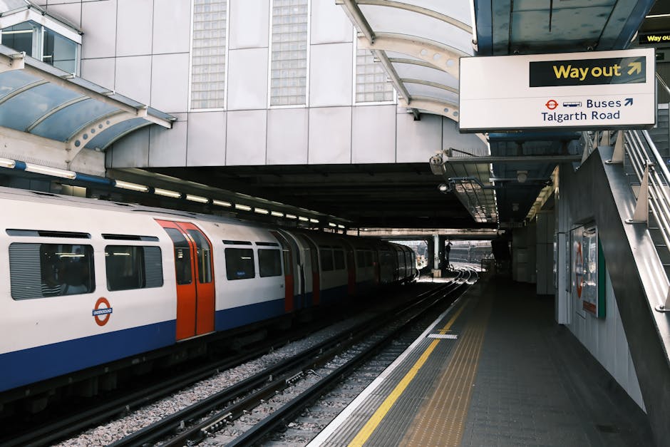 A nighttime exterior view of Edgware Underground station, featuring the illuminated roundel sign with a red circle and blue bar displaying 'UNDERGROUND' in white letters, mounted on a brick wall. The